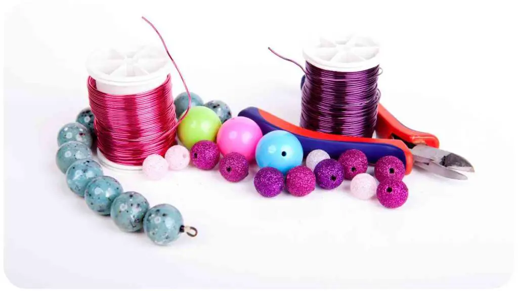 a spool of thread, scissors and beads on a white surface