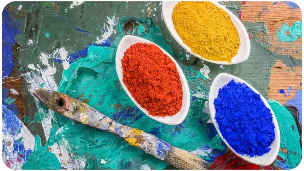 three bowls of colored paint and a brush on a wooden surface