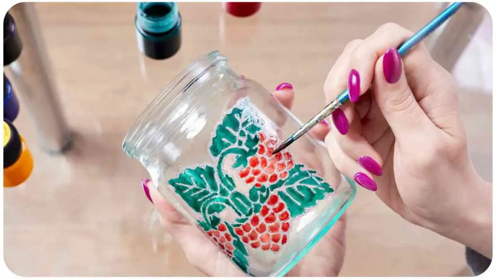 a person is painting a jar with red berries on it