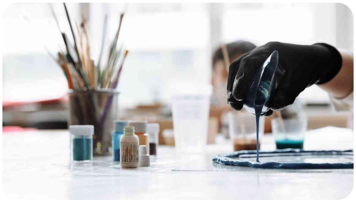a person in a black glove is pouring paint onto a piece of paper
