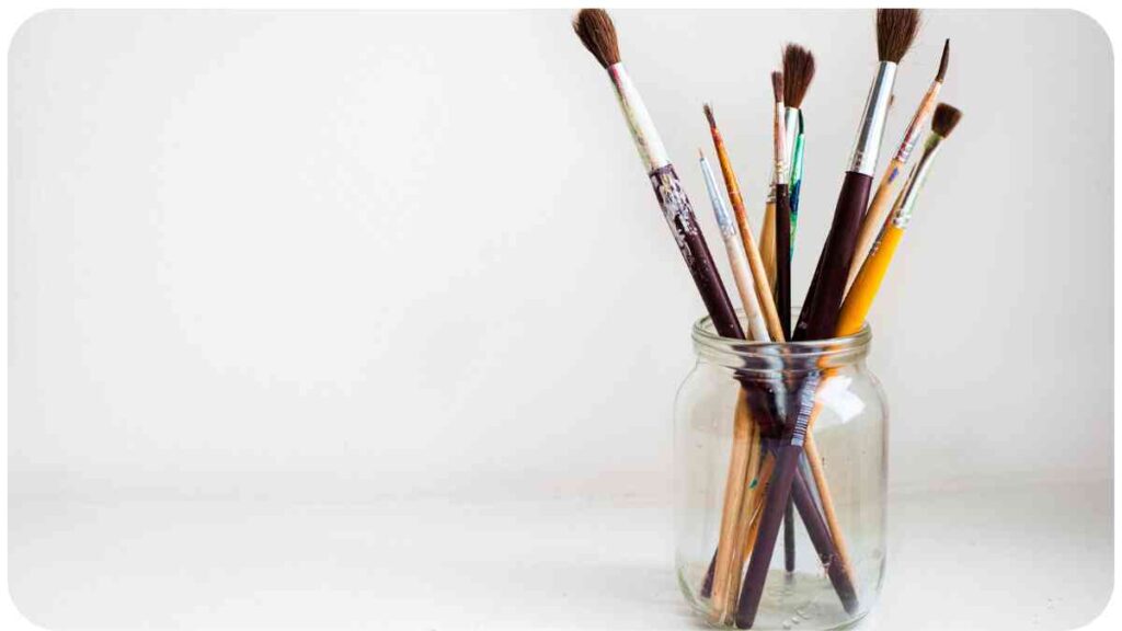 several paint brushes in a glass vase on a white surface